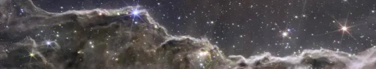 A composite image of the Cosmic Cliffs in the Carina Nebula, created with the Webb telescope’s NIRCam and MIRI instruments. Pinkish brown clouds of gas and dust dominate the foreground of the image, glittering with young stars. Behind the glowing, mountainous clouds, the sky appears navy blue, with shining stars and galaxies.